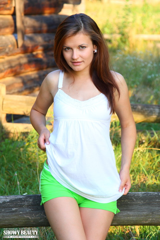 Gorgeous brunette with skinny young body peels down her white blouse and reveals her small boobs before she takes off her neon green shorts and panty as she spreads her legs wide while she sits naked on a wooden fence in a green field. - XXXonXXX - Pic 1