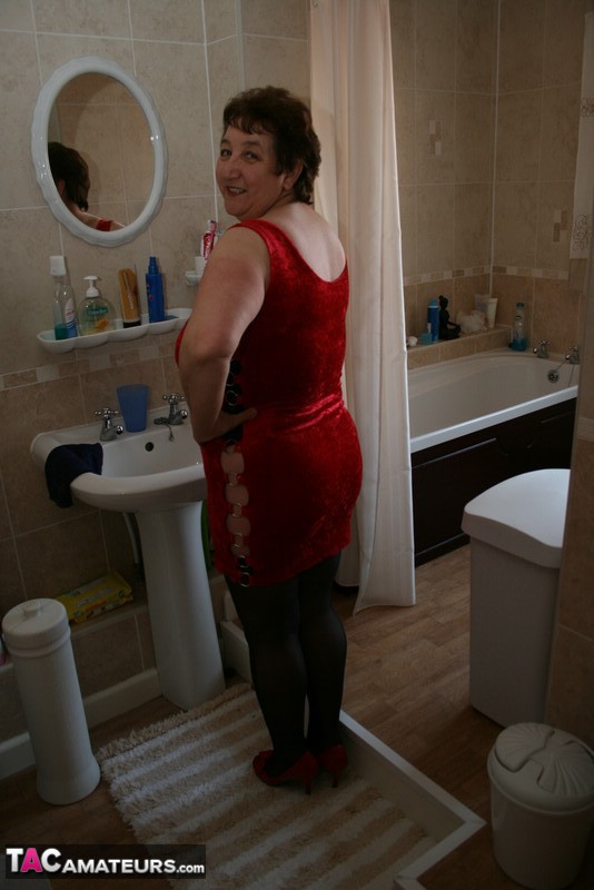 Alluring granny peels off her red dress and seduces with her plus size body in red and black lingerie, black stockings and red high heels in different poses in the bathroom. - XXXonXXX - Pic 2