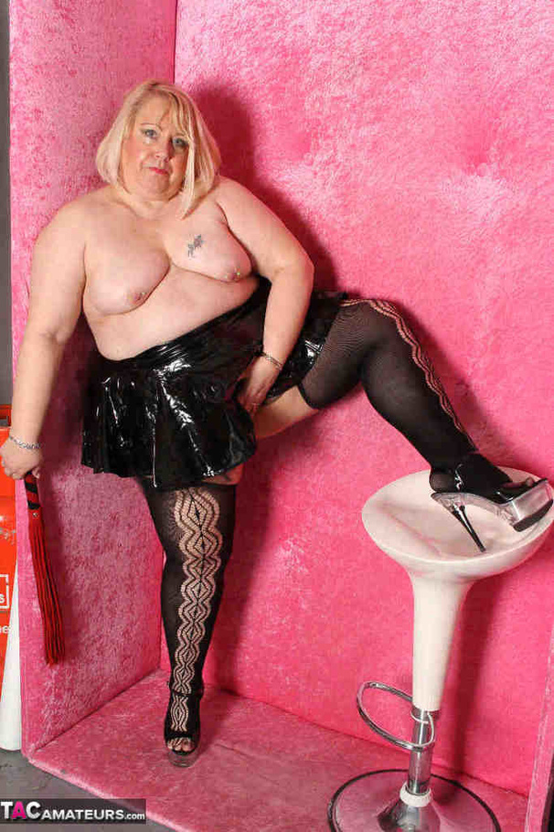 Big blonde in black leather outfit and black stockings stripteasing by the pink wall and showing her pierced vagina - XXXonXXX - Pic 13