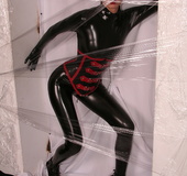 Sexy brunette in black latex jumpsuit takes on red mask