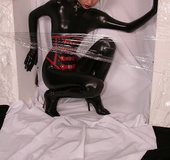 Sexy brunette in black latex jumpsuit takes on red mask