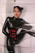 Sexy brunette in black latex jumpsuit takes on red mask
