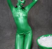 Busty babe in green latex jumpsuit posing with a bowl