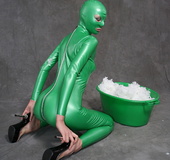 Busty babe in green latex jumpsuit posing with a bowl