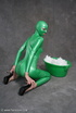 Busty babe in green latex jumpsuit posing with a bowl