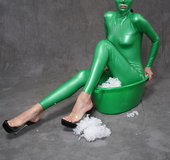 Busty babe in green latex jumpsuit posing with a bowl