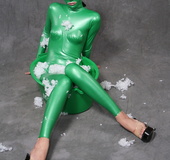 Busty babe in green latex jumpsuit posing with a bowl
