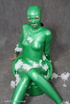 Busty babe in green latex jumpsuit posing with a bowl