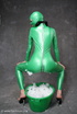 Busty babe in green latex jumpsuit posing with a bowl