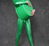 Busty babe in green latex jumpsuit posing with a bowl