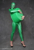 Busty babe in green latex jumpsuit posing with a bowl
