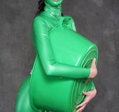 Busty babe in green latex jumpsuit posing with a bowl