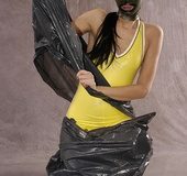 Masked girl in yellow latex comes out of a black sack and reveals her