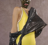Masked girl in yellow latex comes out of a black sack and reveals her