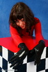 Brunette bombshell in red latex jumpsuit posing with a checked cube