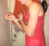 Young crossdresser in red negligee and black pantyhose ties hands to jerk