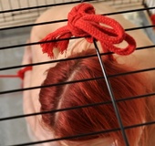 Bound and locked in a cage, a red haired bitch teases with her fat juicy
