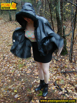 Shy teen wrapped up in a hooded black coat bends down to piss freely in the woods - Picture 1