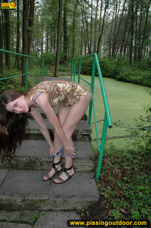 Young innocent looking chick raises short skirt to pee on stone tiles in park - Picture 1