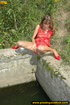 Lady in red with hot small tits hangs up on stone ledge to pee in water