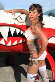 Chick in red polka dot lingerie poses by an airplane.