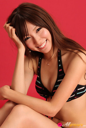 Lady in a black bikini with stripes poses against a red background. - Picture 10