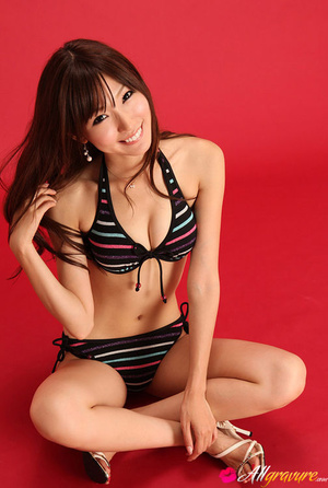 Lady in a black bikini with stripes poses against a red background. - Picture 13