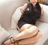 Tart in a black dress and heels poses bound on the sofa.