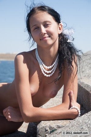 Juicy betty wearing a white necklace poses naked by the water. - Picture 7