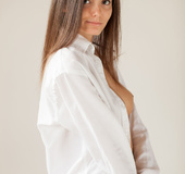 Wicked lady in a white shirt and panties poses in front of a white wall.