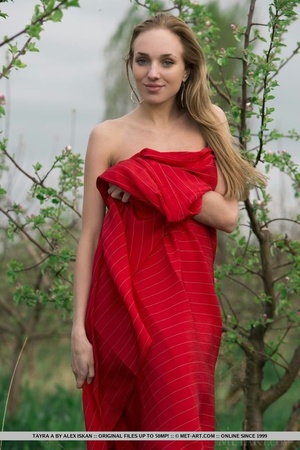Betty wrapped in red fabric poses nude on a grassy field. - Picture 1