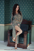 Tramp in a patterned dress sits nude on a green armchair.