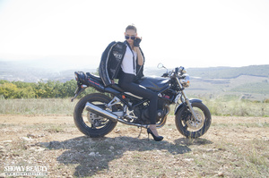 Biker chick in a leather jacket, white shirt and tight pants touches her twat on the bike. - Picture 2
