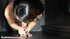 Tattooed chick is on her knees holding a huge cock at a hole and sucks
