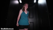 Beautiful babe wearing blue shirt and black shorts is on a black and brown chair and tells that she is a cock worshipper before she kneels down and grabs a dick of a stranger behind a black wall then sucks it and its balls.