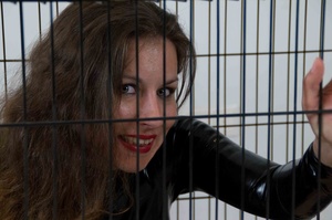 Hazel eyed brunette wearing bright lipstick and shiny latex suit is made to enter a small cage - Picture 5