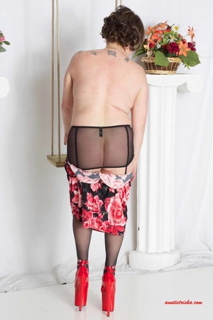 Sweet granny slowly peels off her black, red and white floral dress then reveals her giant boobs before she lets her pussy peek while she sits on a swing wearing her black stockings with black and pink suspenders and red high heels. - XXXonXXX - Pic 10