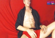 Old dude lays down and smokes a cigarette on a red bed wearing a black robe before he pulls his big cock out of his red and black brief.