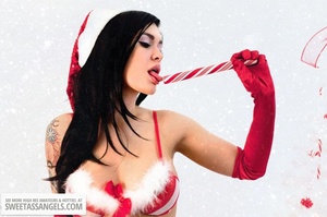 Luscious chick with tattoos displays her smoking hot body wearing her red and white x-mas hat, gloves, stockings and boots before she takes off her red and white lingerie and expose her hot boobs then rubs her pussy by a white x-mas tree. - Picture 11