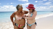 Hot granny in rainbow colored bikini pose her fat body on the beach with another mature hottie in blue and white stripe bikini before they pull down their bras and expose their soggy breasts.