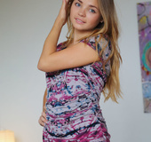 Delightful skank in an abstract print shirt sits naked on a grey sofa.