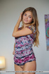 Delightful skank in an abstract print shirt sits naked on a grey sofa.