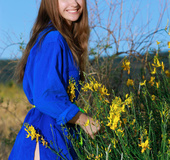 Incredible gal takes off her blue robe by a bush with yellow flowers.