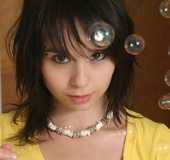 Foxy babe blowing bubbles while she takes off her yellow shirt and display