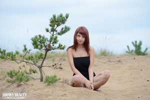 Foxy redhead peels off her black shirt then bares her perfect boobs before she strips down her black panty and shows her indulging pussy as she pose naked outdoor on the sands. - Picture 1