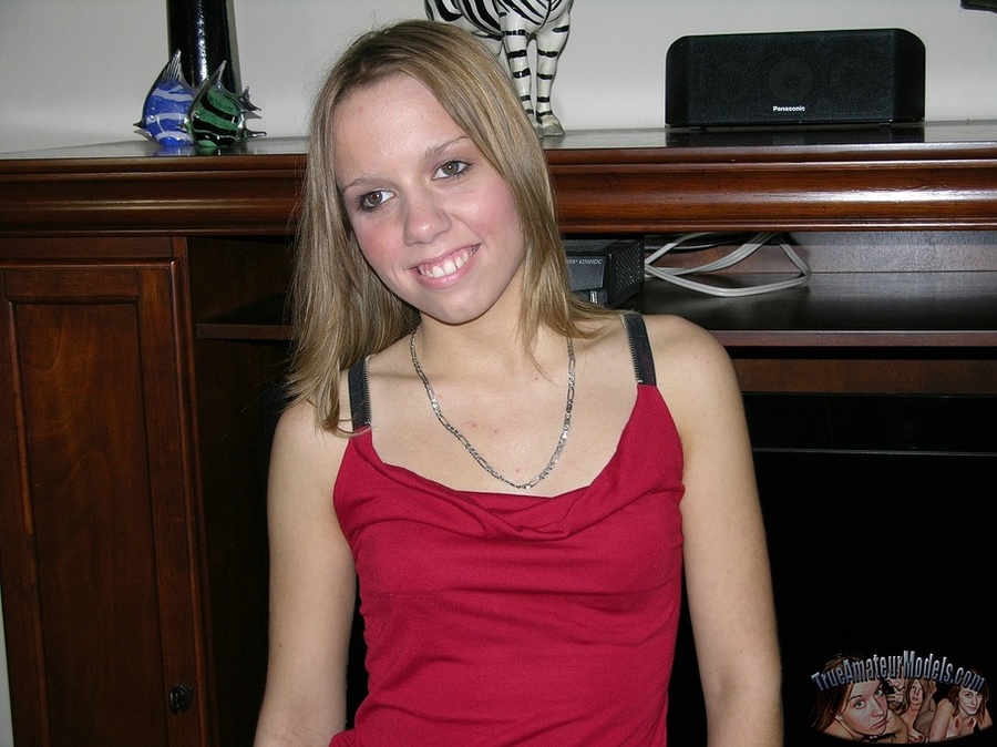 Foxy blonde sits on a gray couch wearing her sexy red blouse and black shorts before she strips them off piece by piece and expose her skinny body with tiny juggs and shaved pussy on a gray couch, stairway and wooden chairs. - XXXonXXX - Pic 2