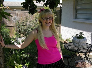 Cute blonde sits on a black chair outdoor wearing black glasses before she goes inside and removes her pink shirt, purple and pink bra, black skirt, panty, pink socks and black shoes. - Picture 2