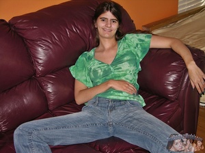 Skinny babe pulls down her jeans and show her clean shaved pussy before she takes off her green and white shirt and reveals her tiny boobs as she lays naked on a brown couch, white and gray striped bed and black chair. - Picture 1