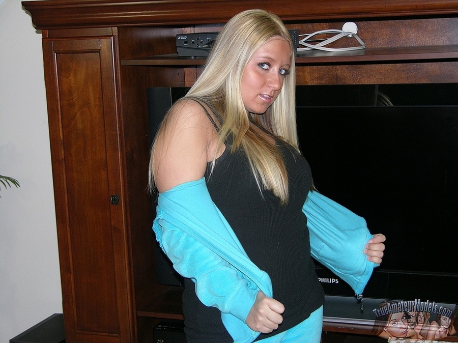 Blonde bombshell seduces as she slowly strips off her turquoise jacket and jogging pants and displays her big ass then takes off her black shirt and expose her huge juggs and indulging pussy in different poses on a gray couch, wooden chair and white bed. - XXXonXXX - Pic 3