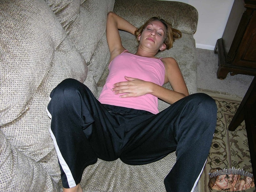 Beautiful babe sits and lays on a gray couch and teases with her steaming hot body before she peels off her pink shirt, black jogging pants and thong then reveals her tiny tits and ravishing pussy on a gray couch and red bed before she holds a hard cock then wanks it on a pink and blue floral couch. - XXXonXXX - Pic 3